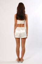 Back view of a woman wearing white satin shorts with an elastic waist and white crop top.