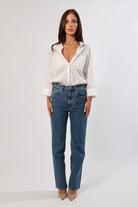 Woman in a white cotton long sleeve pocket shirt and blue jeans.