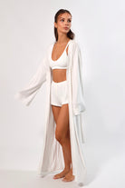 Woman in white maxi robe with bell sleeves, bra top, and button shorts.