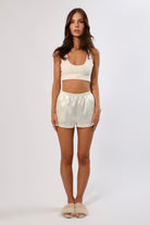 Woman in cream satin lounge set: bra top and elastic waist shorts with pockets.