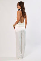 Back view of woman in white satin cowl neck backless top and wide-leg pants.