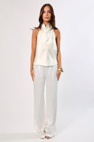 Woman in ivory satin halter top and wide-leg pants. Elegant, minimalist style.