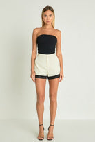 Woman in a black strapless top and cream high-waisted shorts with black satin trim.