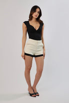 Woman in black bodysuit & high-waisted ivory shorts with black satin hem and pockets.