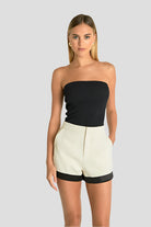 Woman in black top and high-waisted shorts with folded black hem and pockets.