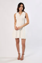 Woman in white sleeveless sweater dress with collar and cinched waist. A-line mini dress.