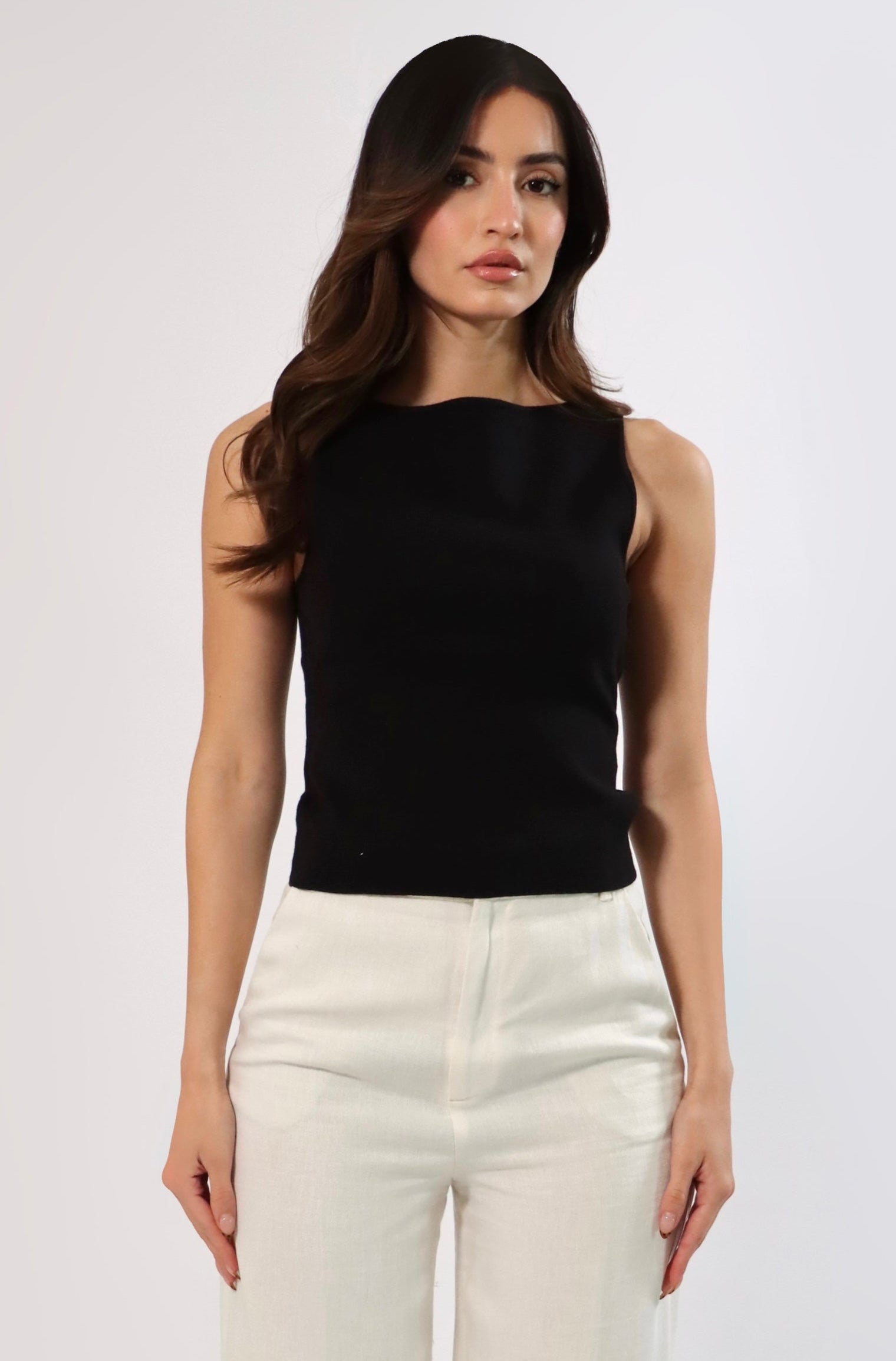 Woman in a black sleeveless top with a boat neck and white pants.
