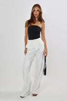 Woman in high-waisted, wide-leg linen pants with button closure and black top.